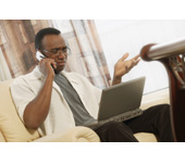 Picture of a man on a cell phone looking at a computer screen